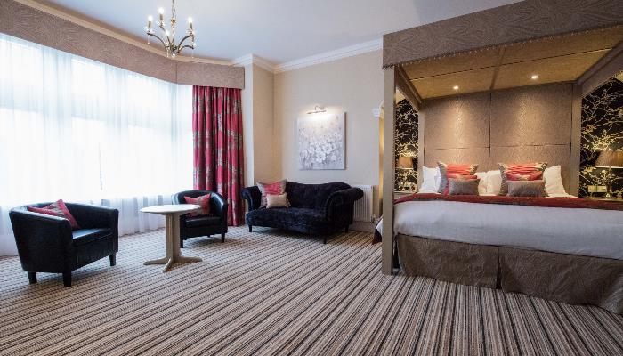 Room with a colourful striped floor & four post bed with white duvet & black leather armchairs by the window