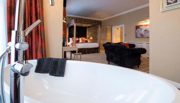 Freestanding bath in a large room with four post double bed & purple velvet sofa