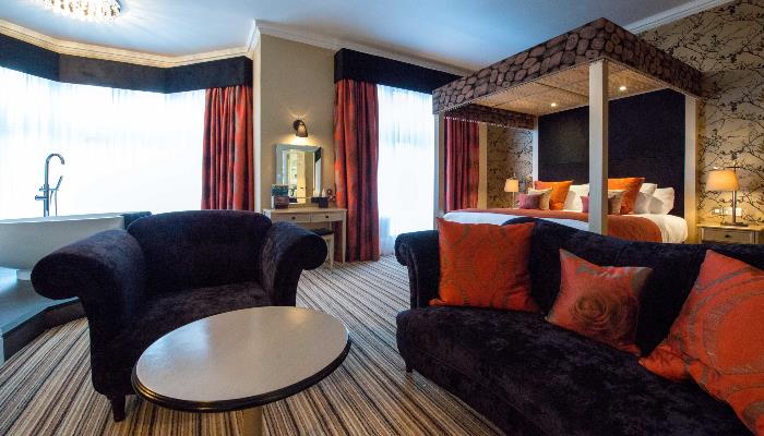 Black velvet sofas with a four post bed in the background & freestanding bath