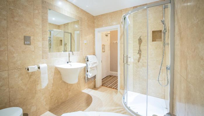 Brightly lit bathroom with large sink, mirror, shower & light brown marbled tiled wall