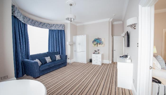 Large living area with colourful striped carpet, blue sofa in front of large bay window with blue curtains