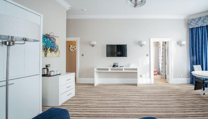 Large room with colourful striped carpet, white walls & furniture & mounted television