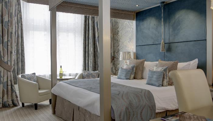 Four post double bed with beautiful blue headboard & cream armchairs positioned by a big bright window
