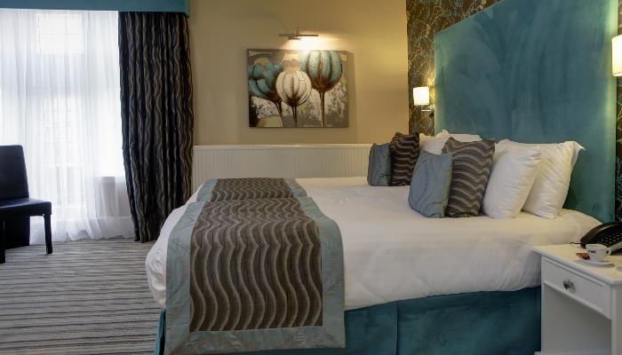 Double bed with white duvet, green & brown blacket over the top & green marbled headboard