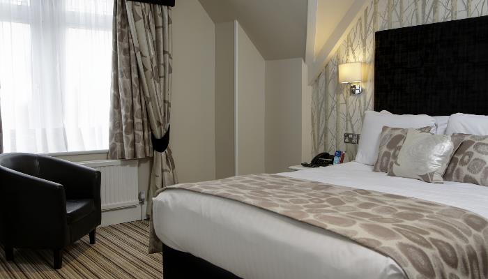 Double bed with white duvet, brown spotted blanket & a black headboard. Black leather armchair in the corner. Light green painted walls.