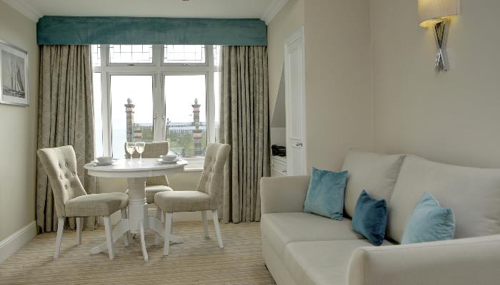 Cream coloured living area with large sofa, dining table & three chairs in front of a large window