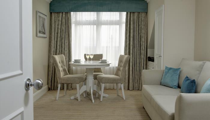 Cream coloured living area with large sofa, dining table & three chairs in front of a large window