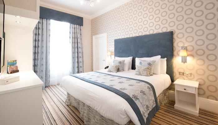 Bright room with double bed with white duvet & blue blanket over the top patterned with flowers