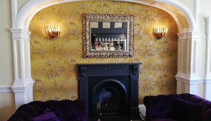 Black fireplace against a floral patterned yellow wall with an ornate mirror mounted above
