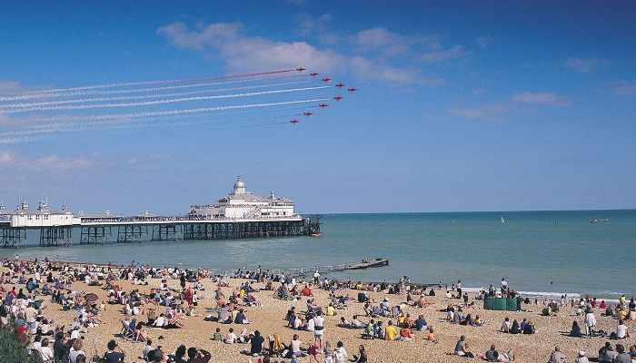 Red Arrows flying over the sea whilst people watch on the beach at Eastbourne Airbourne show